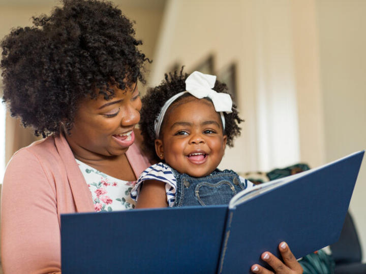 Woman reading to a baby. Both are smiling.