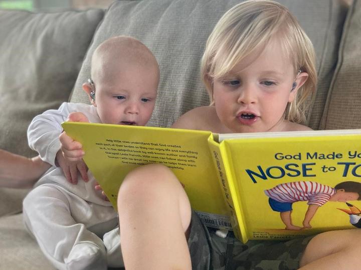 Young child and baby both with hearing aids reading a book