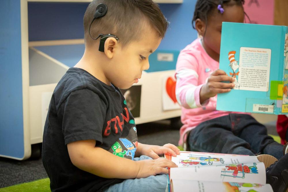 A child with a cochlear implant reading a book with friends.