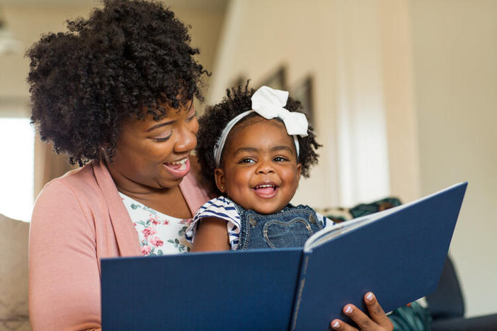 Woman reading to a baby. Both are smiling.